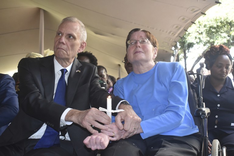 Then-U.S. Ambassador to Kenya Robert Godec (left) helps his wife, Lorri Godec Magnusson, hold a candle during the 20th commemoration of the 1998 bombing of the U.S Embassy in Nairobi, Aug. 7, 2018. Mrs. Godec was left paralyzed and confined to a wheelchair after the bombing. Credit: AP