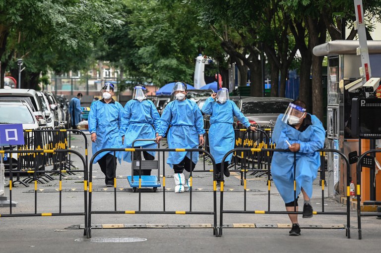 Workers and security guards in protective gear are seen at a cordoned-off entrance to a residential area under lockdown due to Covid-19 restrictions in Beijing, June 14, 2022. Credit: AFP