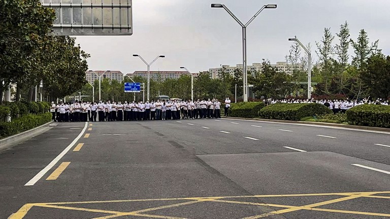 Plainclothes security officers stand on the road as people stage a protest at the entrance to a branch of China's central bank in Zhengzhou in central China's Henan Province on July 10, 2022. Credit: AP