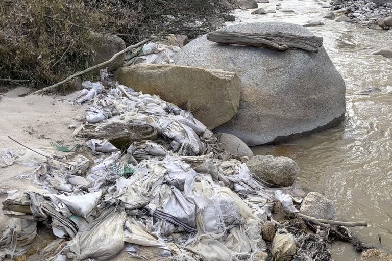 In this early 2022 image from video, a creek in Myanmar's Kachin state is lined with trash, pipes and other construction materials from a former rare earth mining site. Local villagers have said water from the creek is no longer usable for drinking or growing crops and that their skin itches after being exposed to water near rare earth mining sites. Credit: Global Witness via AP
