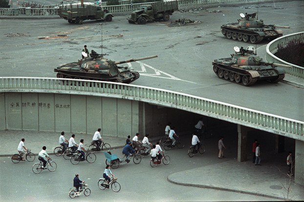 Bicycle commuters pass under an overpass where Chinese army tanks are positioned in Beijing, two days after the Tiananmen Square massacre, June 6, 1989. (Vincent Yu/AP)